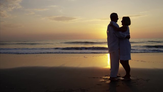 Silhouette retired Caucasian couple dancing on the beach at sunset