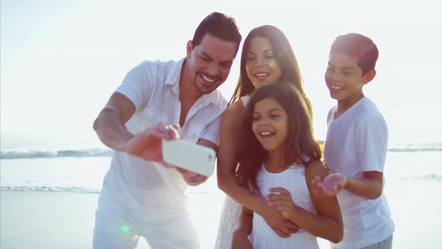 Young Spanish family taking selfie on mobile on beach holiday