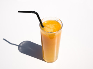 Refreshing glass of delicious orange juice on plain white table background with black straw.