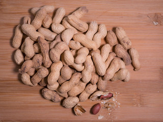 Pile of peanuts in shell with one shell opened, on natural wooden background. Top down view.