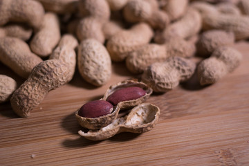 Pile of unshelled whole peanuts with one opened peanut in the foreground on a natural wooden surface table.