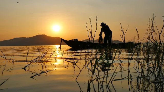 Silhouette scene of Fisherman on boat fishing with a fishnet. He use old traditional fishing equipment for fishing in The lake. Bang Phra Lake - Eastern of Thailand