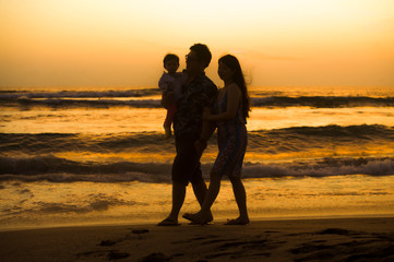 Fototapeta premium silhouette of young happy and beautiful Asian Chinese couple holding baby girl daughter walking on sunset beach enjoying together romantic summer holidays