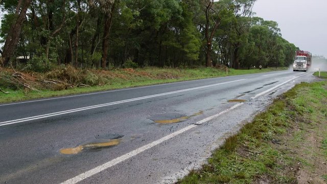 Heavy logging truck on damaged highway filled with potholes.