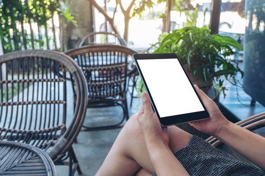 Mockup image of a woman holding black tablet pc with blank white screen while sitting in outdoor