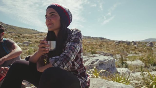 Young woman drinking coffee and resting with friend during hike. Young people taking a break during hike.