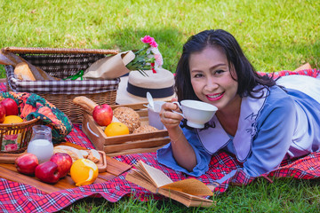 Young Asian woman relax time in park.In the morning She is  lying on the grass.  smile and  laugh. beside picnic basket. Photo lifestyle and picnic idea.