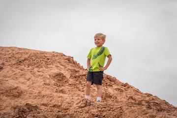 A little boy standing on red rock hillside and looking into the distance with his hands on his hips