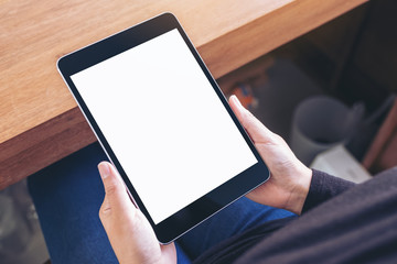 Top view mockup image of a woman holding black tablet pc with blank white screen while sitting on a chair