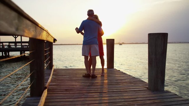 Silhouette of romantic mature Caucasian couple dancing on the wharf at sunrise