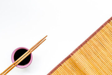 Chinese meal concept. soy sauce in bowl near chopsticks and bamboo table mat on white background...