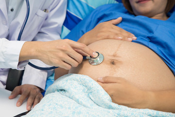 Fototapeta na wymiar Pregnant woman with doctor in hospital. Doctor using stethoscope examining pregnant girl. Mother,baby and family concept