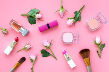 Obraz na płótnie Canvas Decorative cosmetics layout. Pink tones of lipstick, bulk, eyeshadow, perfume among rose flowers on pink background top view