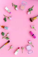 Rose, pink decorative cosmetics frame. Lipstick, bulk, eyeshadow and small rose flowers on pink background top view copy space