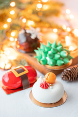 Fototapeta na wymiar Mini mousse pastry desserts covered with velour or glaze. Garland lamps bokeh on background. Modern european cake. French cuisine. Christmas theme.