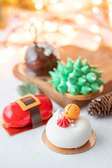 Mini mousse pastry desserts covered with velour or glaze. Garland lamps bokeh on background. Modern european cake. French cuisine. Christmas theme.
