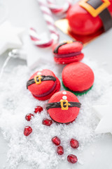 Obraz na płótnie Canvas Funny cookie in the form red santa belly on gray table sprinkled with snow. Modern european French cuisine. Christmas theme, Merry Christmas card. New year mood. Variety of sweet macaroons.