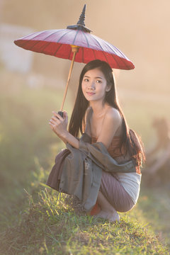 Asian cute girl wearing Thai traditional dress with red umbrella and with Lanna style,vintage style,Chaingmai, Thailand. Most of Thai women wearing this dress on Friday.