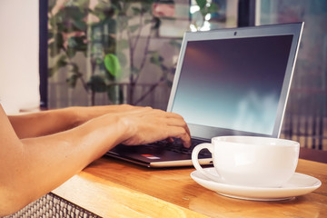 Man hands typing on laptop on wooden table with a cup of hot coffee ,soft focus on coffee cup  with vintage toned..