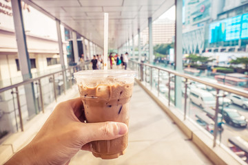 Holding Iced Coffee Latte in Hand while Walking through overpass in the Morning background