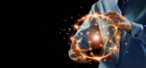 Abstract science, hands holding atomic particle, nuclear energy imagery and network connection on dark background. - obrazy, fototapety, plakaty