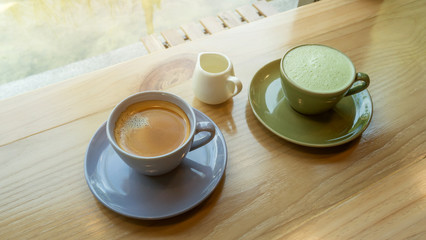 A cup of hot coffee and hot green tea on a wooden table in a morning.