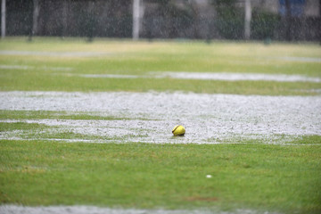 A fresh green softball left on a raining field waiting for a league match to begin while the field is full with water and no player.