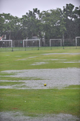 A fresh green softball left on a raining field waiting for a league match to begin while the field is full with water and no player.