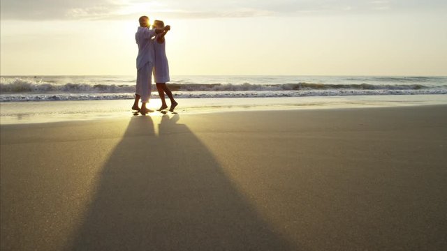 Silhouette of retired Caucasian couple dancing on the ocean beach at sunset