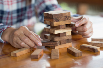 hand of businessman pulling out or placing wood block on the tower. plan and strategy in business.  Risk management, Challenge In Business Concept.
