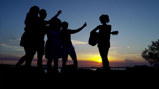 Silhouette of young friends dancing by the ocean at sunset