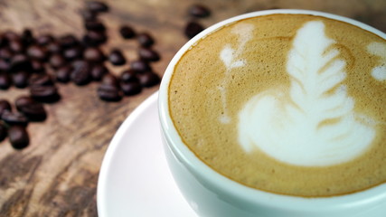 Cappuccino or latte art coffee. Free hand pouring some foam of milk on top. A white ceramic cup on the wood table with some coffee beans. The best food and drink in the world. Fresh energy everyday.