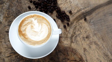 Cappuccino or latte art coffee. Free hand pouring some foam of milk on top. A white ceramic cup on the wood table with some coffee beans. The best food and drink in the world. Fresh energy everyday.
