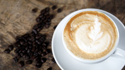 Cappuccino or latte art coffee. Free hand pouring some foam of milk on top. A white ceramic cup on the wood table with some coffee beans. The best food and drink in the world. Fresh energy everyday.