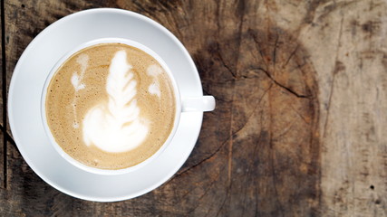 Cappuccino or latte art coffee. Free hand pouring some foam of milk on top. A white ceramic cup on the wood table with some coffee beans. The best food and drink in the world. Fresh energy everyday.