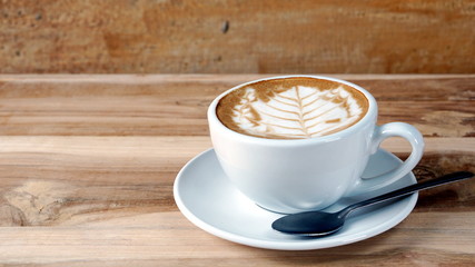 Cappuccino or latte art coffee. Free hand pouring some foam of milk on top. A white ceramic cup on the wood table with some coffee beans. The best food and drink in the world. Fresh energy everyday.