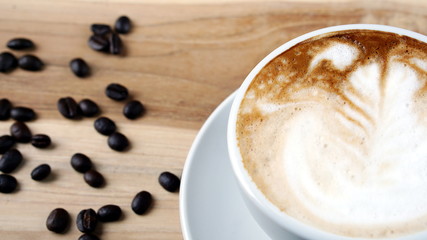 Cappuccino or latte art coffee. Free hand pouring some foam of milk on top. A white ceramic cup on the wood table with some coffee beans. The best food and drink in the world. Fresh energy everyday.