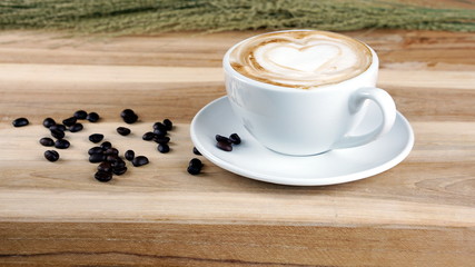 Cappuccino or latte art coffee. Free hand pouring some hearts of milk on top. A white ceramic cup on the wood table with some coffee beans. The best food and drink in the world. Fresh energy everyday.