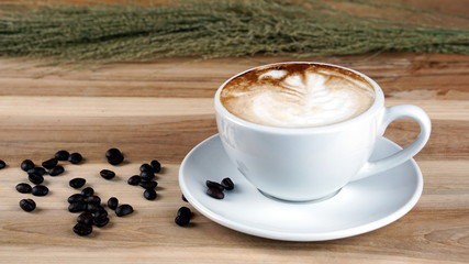 Cappuccino or latte art coffee. Free hand pouring some foam of milk on top. A white ceramic cup on the wood table with some coffee beans. The best food and drink in the world. Fresh energy everyday.