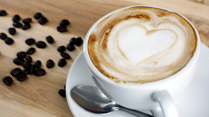 Cappuccino or latte art coffee. Free hand pouring some hearts of milk on top. A white ceramic cup on the wood table with some coffee beans. The best food and drink in the world. Fresh energy everyday.