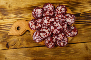 Sliced salami sausage on cutting board on wooden table. Top view