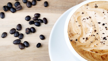 Cappuccino or latte art coffee. Free hand pouring some foam of milk on top. A white ceramic cup on the wood table with some coffee beans. The best food and drink in the world. Fresh energy everyday.