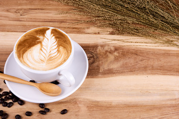 Hot cappuccino or latte art coffee. A cup of coffee on the wooden table with roasted beans. Morning breakfast with coffee. Flowers shape created by pouring steamed milk.