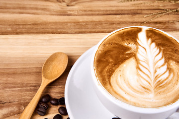 Hot cappuccino or latte art coffee. A cup of coffee on the wooden table with roasted beans. Morning breakfast with coffee. Flowers shape created by pouring steamed milk.