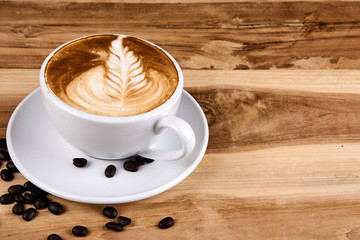 Hot cappuccino or latte art coffee. A cup of coffee on the wooden table with roasted beans. Morning breakfast with coffee. Flowers shape created by pouring steamed milk.