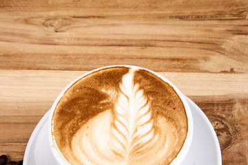 Hot cappuccino or latte art coffee. A cup of coffee on the wooden table with roasted beans. Morning breakfast with coffee. Flowers shape created by pouring steamed milk.
