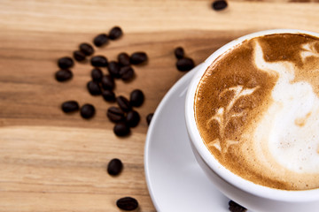 Hot cappuccino or latte art coffee. A cup of coffee on the wooden table with roasted beans. Morning breakfast with coffee. Abstract shape created by pouring steamed milk.