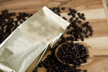 Coffee bag and packaging. The gold foil bag on the wood table with dark roasted coffee beans.