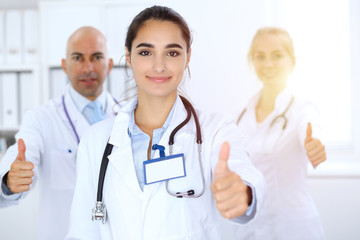 Fototapeta premium Group of doctors showing OK or approval sign with thumb up. High level and quality medical service, best treatment and patient care concept