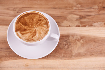Hot cappuccino or latte art coffee. A cup of coffee on the wooden table with roasted beans. Morning breakfast with coffee. Hearts shape created by pouring steamed milk.